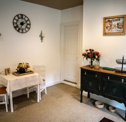 A corner dining area with a small table and two chairs a sideboard with flowers and wall clock at Anvil Lodge in Goulceby near Louth