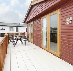 An outdoor patio with a table and four chairs next to a brown wooden building with double glass doors at Jolie in Hunstanton