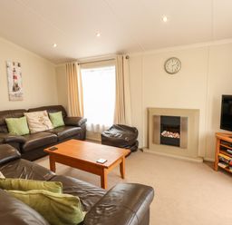 A living room with brown leather sofas a wooden coffee table a television on a stand and a fireplace at Jolie in Hunstanton