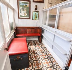 A small seating area with a wooden bench and a chest with red cushions and framed posters on the wall at The Merchant's Store in Kilrush Country Clare