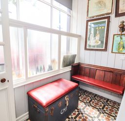 A small seating area with a wooden bench and a chest with red cushions and framed pictures on walls at The Merchant's Store in Kilrush Country Clare