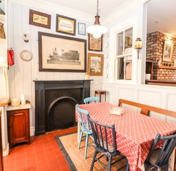A dining area with a red patterned tablecloth on a table surrounded by blue and wooden chairs a black fireplace and framed pictures on white paneled walls at The Merchant's Store in Kilrush Country Clare