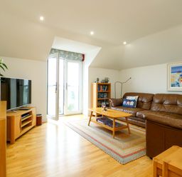 A living room with a sofa and television at Maelog, 14 Tides Reach Rhosneigr