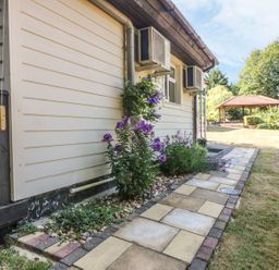 A side view of a house with flower plants along a paved walkway and a garden area with a gazebo at Badger View in Culverstone Green near Chatham