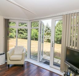 A room with a chair a table a television and glass doors leading to a garden at Badger View in Culverstone Green near Chatham