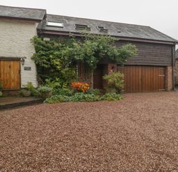 A gravel driveway in front of a house with wooden doors and climbing plants at The Old Bakery in Crowcombe