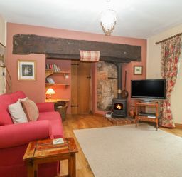 A living room with a red sofa a wood stove television and floral curtains at The Old Bakery in Crowcombe