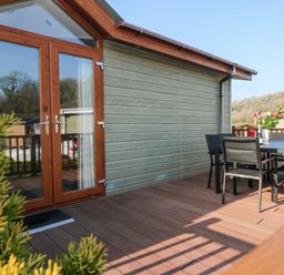 A wooden deck with a table and chairs outside a cabin with glass double doors at Tranquillity - Heritage Park Stepaside near Kilgetty