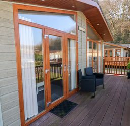 A wooden deck with black chairs potted plants and glass doors at Tranquillity - Heritage Park in Stepaside near Kilgetty