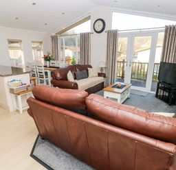 A living room with brown leather sofas a small coffee table and a dining area at Tranquillity - Heritage Park in Stepaside near Kilgetty