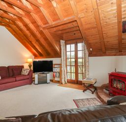 A living room with a red wood stove sofa television and glass door at Floras Barn in Crowcombe