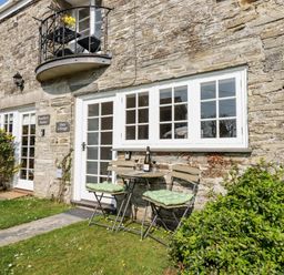 A stone cottage exterior with white framed windows and a small patio table with two chairs on grass at Slate Cottage Tredethy near Bodmin Moor