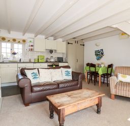 A living room with a brown leather sofa, wooden coffee table, armchair, dining table with green tablecloth and kitchen area at Slate Cottage in Tredethy near Bodmin Moor