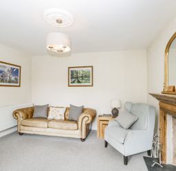 A living room with a leather sofa and armchair beside a wooden fireplace and framed pictures on the wall at Viaduct House in Lydbrook