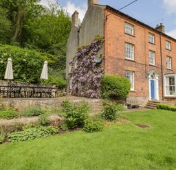 A brick house with a garden table and chairs on a patio and plants growing on the side at Viaduct House in Lydbrook