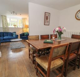 A dining area with a wooden table and eight chairs next to a living room with blue sofas and a coffee table at Aldrich Cottage in Radstock