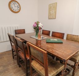 A dining room with a wooden table and chairs and a clock on the wall at Aldrich Cottage in Radstock