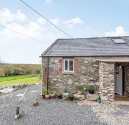 Stone cottage exterior with potted plants and outdoor seating on gravel at Celyn Farm Cottage in Deiniolen near Llanberis