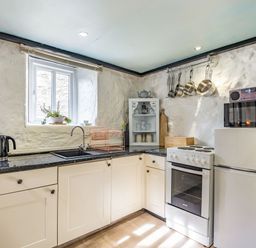 A kitchen with a stove fridge microwave toaster kettle and hanging pots at Celyn Farm Cottage Deiniolen near Llanberis