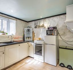 A kitchen with white cabinets a stove a refrigerator a microwave and a sink at Celyn Farm Cottage in Deiniolen near Llanberis
