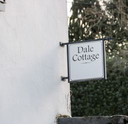 A white wall with a hanging sign that reads Dale Cottage with trees in the background at Dale Cottage in Llanrwst