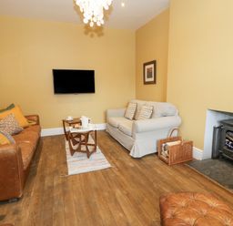 A living room with two sofas a wood burning stove a television and a small table at Dale Cottage in Llanrwst