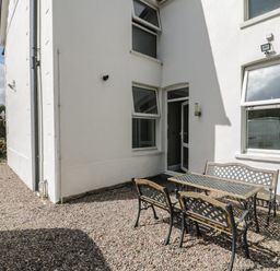 An outdoor patio area with a metal table and benches on gravel outside a white building at Dale Cottage in Llanrwst