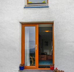 A wooden framed glass door in a white wall with two potted plants outside at Pen Y Graig in Talysarn