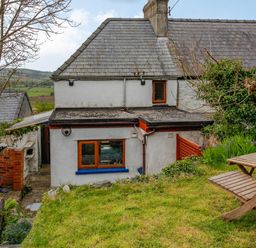 The rear view of a two storey house with a stone slate roof and garden with wooden outdoor furniture at Pen Y Graig in Talysarn