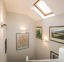 A stairwell with framed pictures on the walls and a skylight window at Rothay 17 in Ambleside