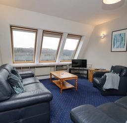 A living room with leather sofas a wooden coffee table and slanted windows at Rothay 17 in Ambleside