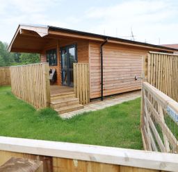 A wooden cabin with a covered porch and fenced yard at Hayfields in Grimston