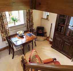 A dining area with a wooden table and chairs next to a window with floral curtains and a cabinet at The Old Cider House in Prestbury near Cheltenham