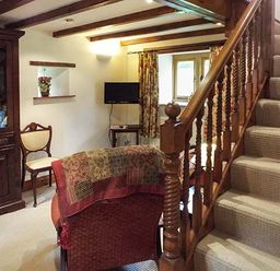 A living room with wooden staircase a cabinet a chair and a television at The Old Cider House Prestbury near Cheltenham