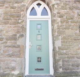 A stone wall with a green door featuring four glass panels and a metal mail slot at No 1 Church Cottages Llanelli