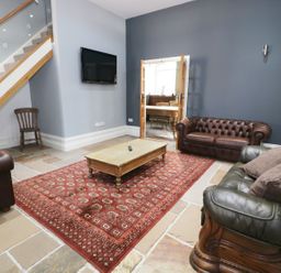 A living room with leather sofas a wooden coffee table a red patterned rug a wall mounted TV and a wooden chair at No 1 Church Cottages in Llanelli