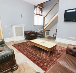 A living room with sofas a wooden coffee table a red patterned rug stairs and a wall-mounted television at No 1 Church Cottages in Llanelli