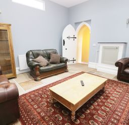 A living room with leather armchairs a wooden cabinet a coffee table and a red patterned rug at No 1 Church Cottages Llanelli
