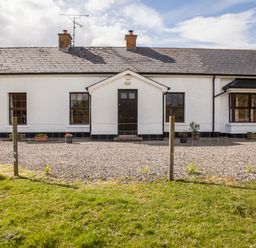 A white single-story house with a black door and windows surrounded by gravel and grass at Shepherds Retreat in Gortin