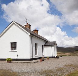 A white house with two chimneys and potted plants on a gravel driveway with hills in the background at Shepherds Retreat in Gortin