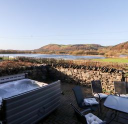 An outdoor patio with a hot tub and table with chairs overlooking a river and hills at Green Hills Farm in Ulverston