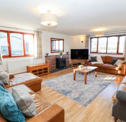A living room with brown leather sofas a wooden coffee table a television and windows with checkered curtains at Green Hills Farm in Ulverston