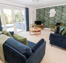 A living room with blue sofas green armchair round wooden coffee table and glass doors with garden view at The Croft in Longhoughton near Alnwick