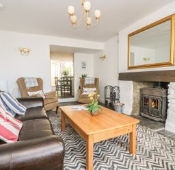 A living room with a leather sofa armchairs a wooden coffee table fireplace and a large mirror at The Watch Below in Polruan