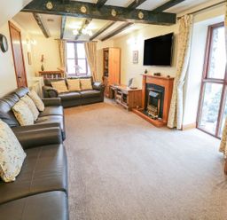 A living room with two leather sofas a fireplace a wall-mounted television wooden furniture and curtains at Bank End Barn Grizebeck