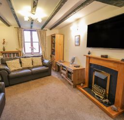A living room with leather sofas a wooden fireplace a wall mounted television and bookshelves at Bank End Barn in Grizebeck