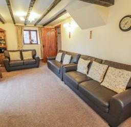 A sitting room with leather sofas cushions wooden furniture and exposed ceiling beams at Bank End Barn in Grizebeck