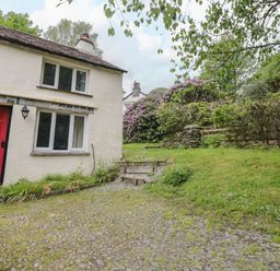 A white house with a red door next to a gravel driveway and grassy garden at Hall Bank Cottage in Rydal near Ambleside
