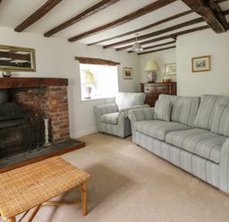 A living room with a striped sofa and armchair a brick fireplace and a wicker coffee table at Hall Bank Cottage in Rydal near Ambleside