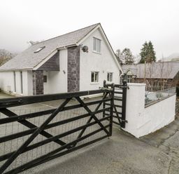 A white house with dark stone accents behind a black wooden gate at Ty Coch in Llanberis